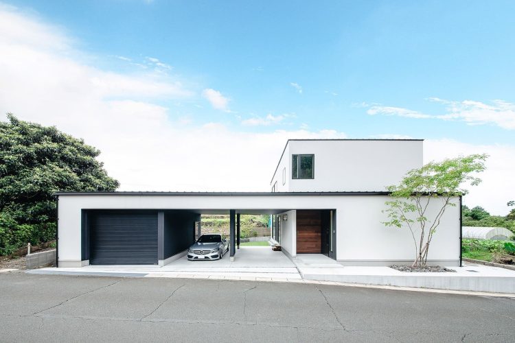 ビルトインガレージに車が駐車された白いモダンな2階建て住宅と青空の下の外観