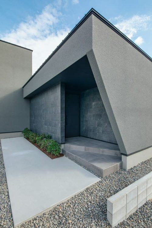 ダンなグレーの外壁と黒いドアが印象的な斜めの壁に囲まれた玄関ポーチ