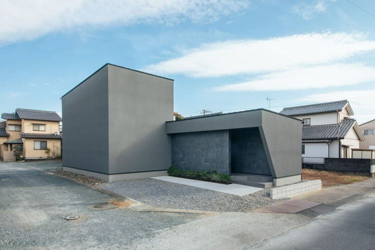 広い砂利の敷地に建つ入口の斜め壁が特徴的なグレーのモダンな箱型住宅