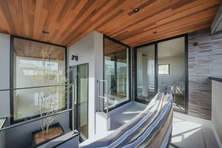 木目の天井と大きな窓に囲まれたハンモックと植栽がある開放的なバルコニー