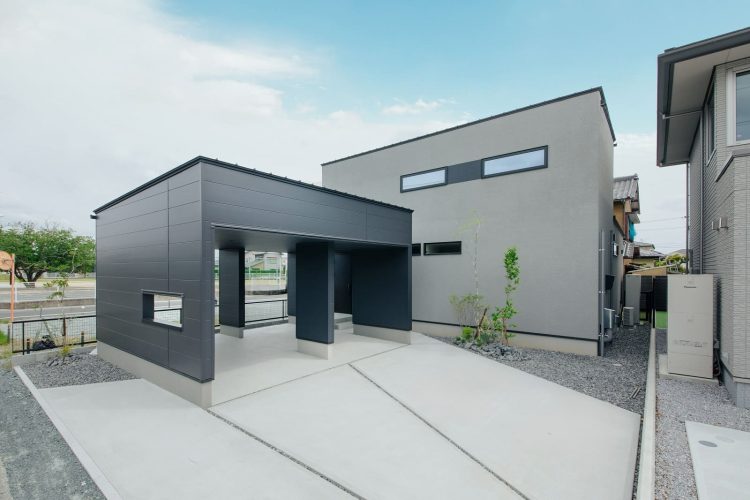 グレーの四角い箱型の建物と黒いカーポートが調和したシンプルモダンな住宅外観