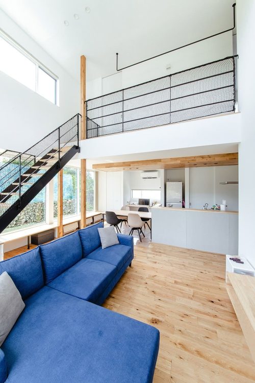 青いソファを置いた吹き抜けリビングと黒い鉄骨階段の上にあるネット遊具スペース