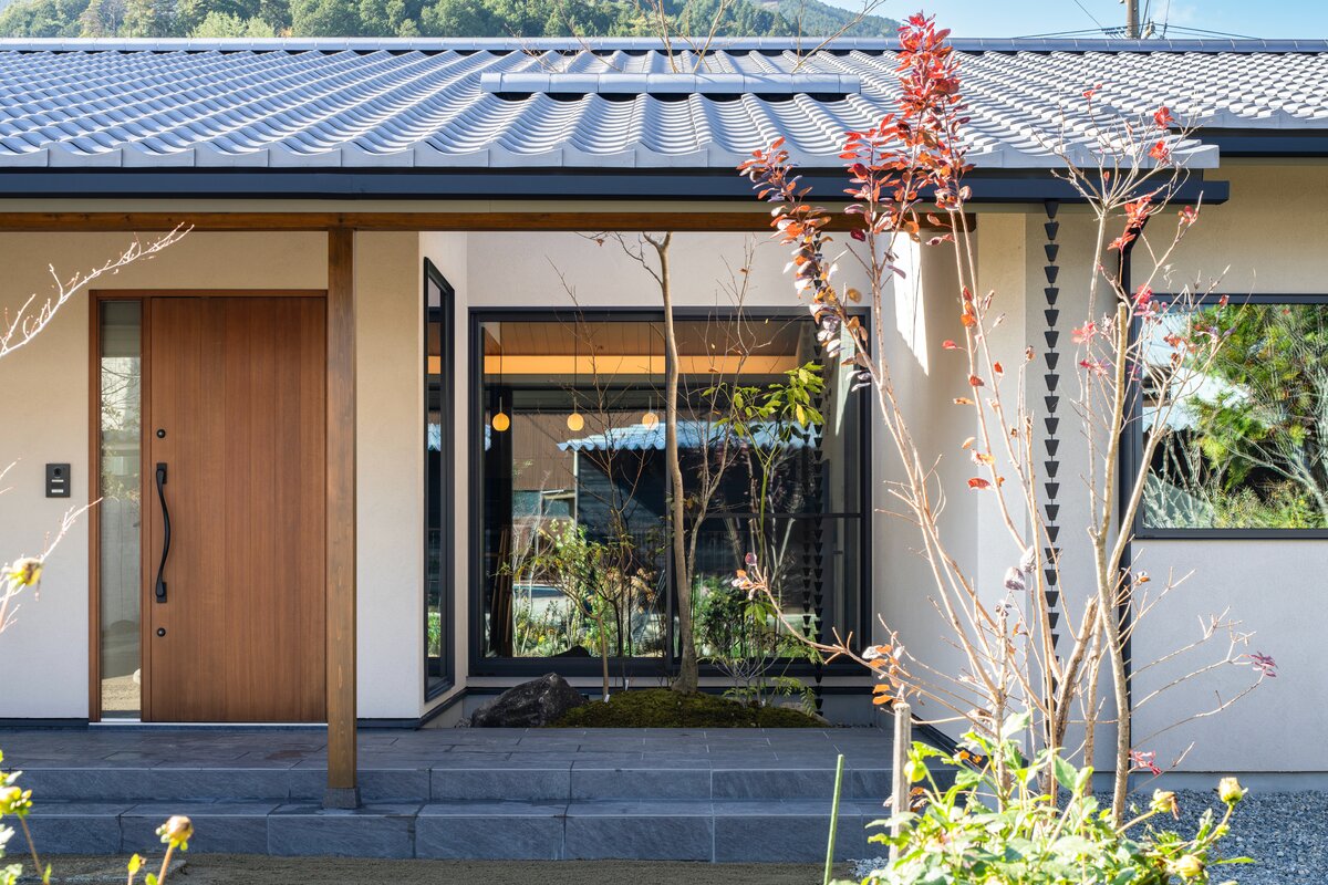 白い外壁と瓦屋根の平屋の玄関アプローチと豊かな植栽
