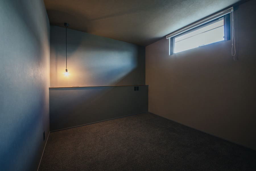 高窓からの光とペンダントライトが照らすカーペット敷きの部屋